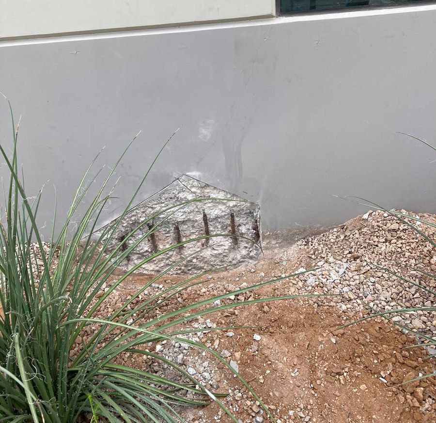 Tilt panel base with concrete broken away and rebar exposed at grade, before repair